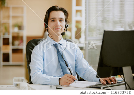 Portrait of Caucasian call center specialist holding pen and ready to type on keyboard in comfortable and modern office while looking at camera 116833738