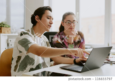 Young Caucasian IT specialist pointing at laptop screen while his female coworker watching carefully 116833797