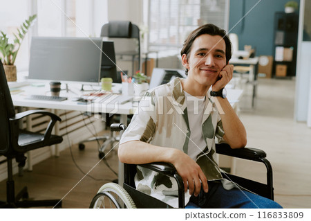 Portrait of smiling Caucasian IT specialist with disability looking at camera while his head based on hand, he in office of modern high-end IT company Portrait of smiling Caucasian IT specialist with disability looking at camera while his head based on hand, he in office of modern high-end IT company 116833809