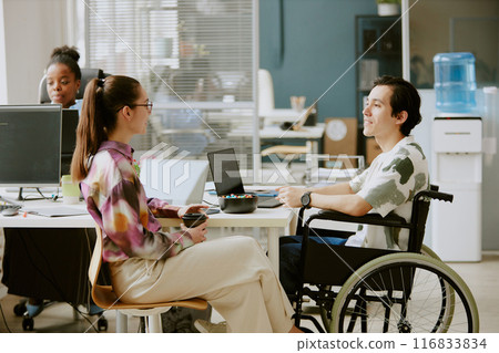 Two Caucasian coworkers having nice conversation while female colleague drinking coffee and her male colleague with disability coding 116833834