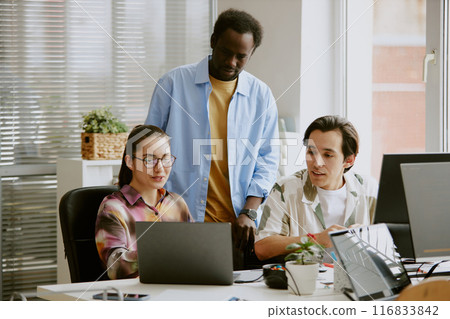 African American teamlead standing between two Caucasian coworkers who showing new project to him 116833842