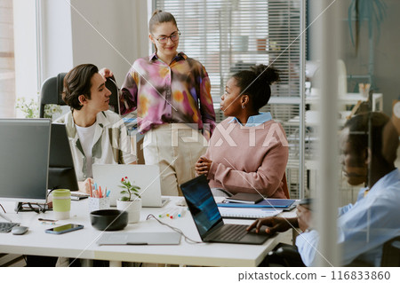 Biracial colleagues chatting in office while their african american coworker using laptop to write codes 116833860