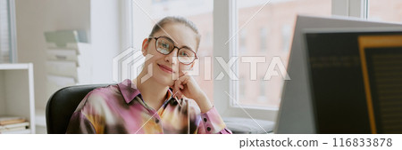 Website header shot of young Caucasian woman leaning on her hand and smiling while sitting in office during her work time 116833878