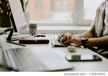 Medium close up of unrecognizable male hands with black watch typing on black keyboard in light office 116833903