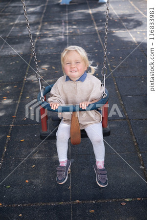 Cute smiling kid girl playing on a swing outdoor on a playground.  116833981