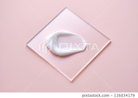 A smear of white cream on a square transparent stand on a pink background. 116834179