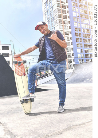 The perfect way to get through these streets, teenager in street clothes stands with a longboard, looks at the camera and smiles. Street culture. The perfect way to get through these streets, teenager in street clothes stands with a longboard, looks at the camera and smiles. Street culture. 116835375