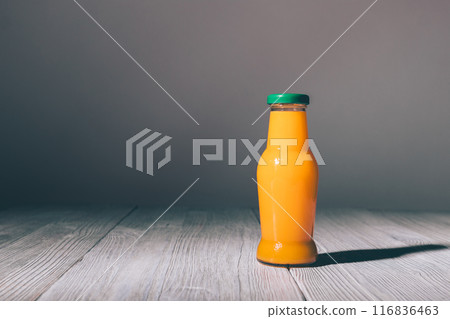 A glass bottle of orange juice is sitting on a wooden table 116836463
