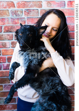 Happy brunette lady in casual wear hugging mudi pet dog, studio background. 116836511