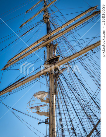 Tall ship mast, rigging, yards against clear sky. Classic sailing vessel with crow's nest, harking back to Age of Sail era Tall ship mast, rigging, yards against clear sky. Classic sailing vessel with crow's nest, harking back to Age of Sail era 116836559