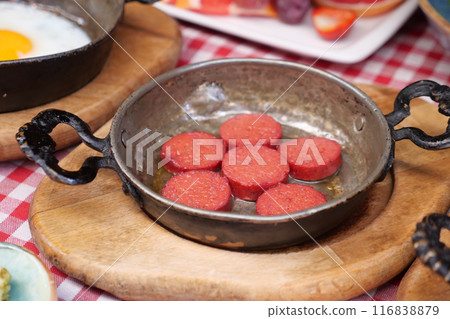 Cooking a dish of breakfast sausage in a pan on a wooden table 116838879