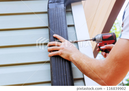 Installation rain gutters on roof with installation of downpipes downspout bends 116839902