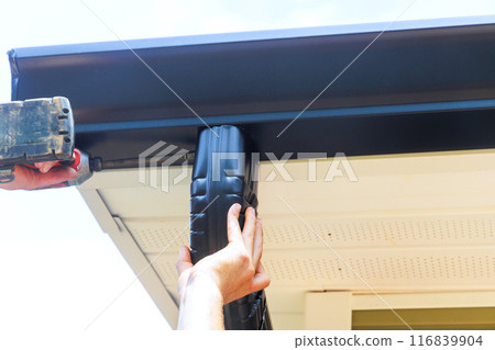 Installing rain gutter on roof, fitting downpipe, downspout bend 116839904