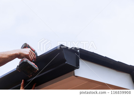 Worker installing rain gutter on roof is mounting downpipe 116839908