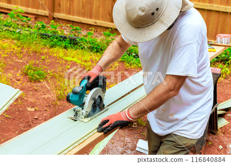 Before installing plastic siding, worker cuts it to required size with hand saw 116840884
