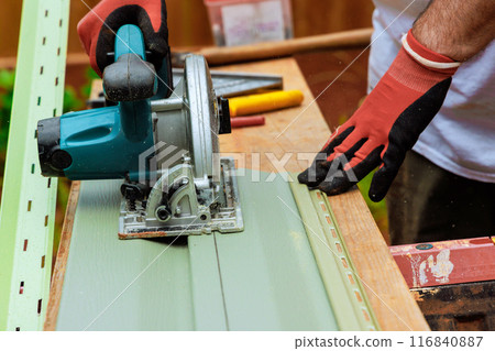 With circular hand saw, worker cuts plastic vinyl siding to required size 116840887