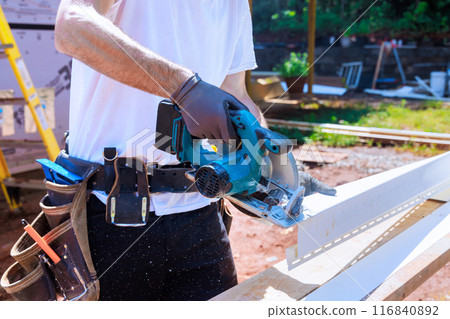 Worker cuts plastic vinyl siding to size before installing it with circular handsaw Worker cuts plastic vinyl siding to size before installing it with circular handsaw 116840892