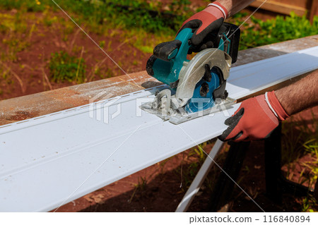 Before installing plastic vinyl siding, worker cuts it with circular handsaw 116840894