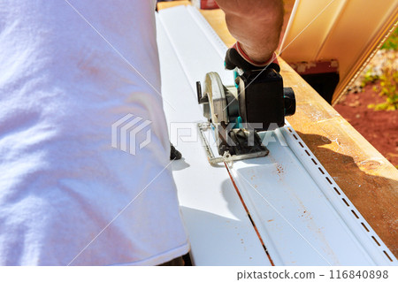 Workers cut plastic vinyl siding to required size before installing it 116840898