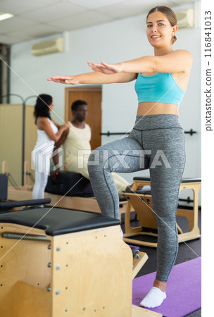 Girl performing set of pilates exercises on reformer in modern fitness studio Girl performing set of pilates exercises on reformer in modern fitness studio 116841013