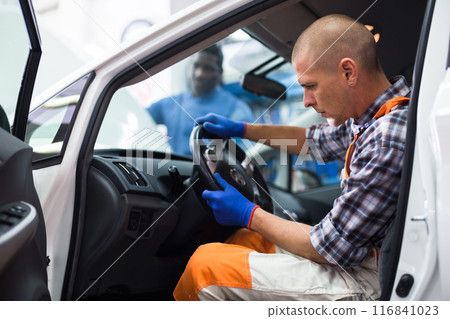 Auto mechanic sitting in broken car and listens to engine operation Auto mechanic sitting in broken car and listens to engine operation 116841023