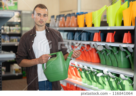 Amateur gardener guy selects watering can for hobby in greenhouse flower-bed 116841064