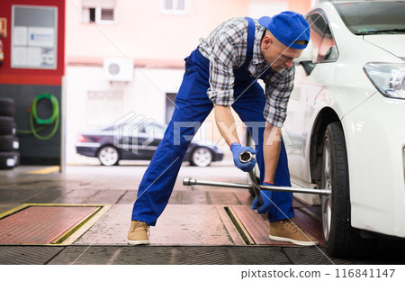Mechanic engaged in replacement of tyre on car wheel in workshop Mechanic engaged in replacement of tyre on car wheel in workshop 116841147
