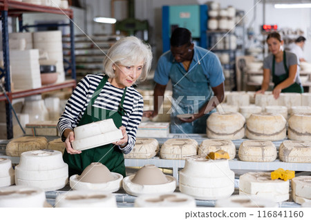Elderly female worker removes half of the gypsum mold. Removal of the first part of clay mold 116841160