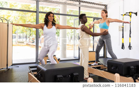 Two women having pilates workout on reformers with trainer Two women having pilates workout on reformers with trainer 116841183