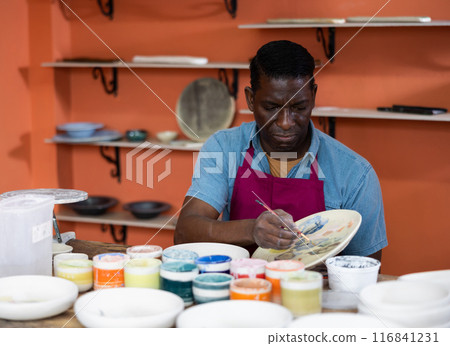 Man ceramist painting new crafted plate Man ceramist painting new crafted plate 116841231