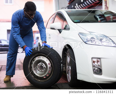 Mechanic engaged in replacement of tyre on car wheel in workshop Mechanic engaged in replacement of tyre on car wheel in workshop 116841311