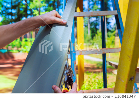 Using scissors, worker cuts plastic vinyl siding to size prior to installation 116841347