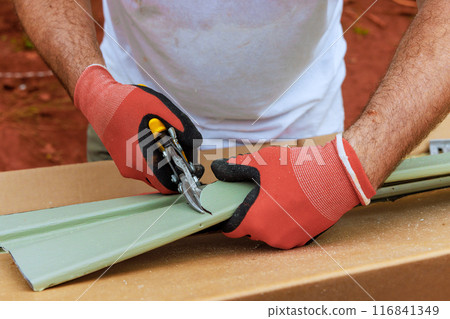 Worker cuts plastic vinyl siding to size with of scissors before installing it 116841349