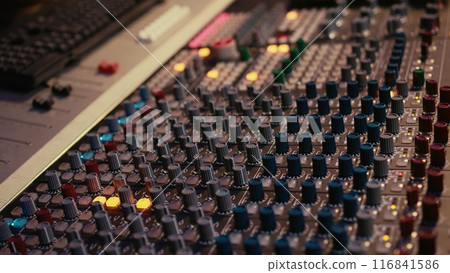 Sound designer manipulating sound effects to enhance tunes on audio recordings, processing and mixing tracks to create a new song. Professional expert works in control room at studio. Camera B. 116841586