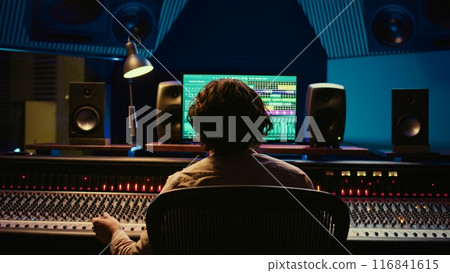 Joyful pleased music producer enjoying his high quality track in control room, finishing project with knobs and sliders. Audio engineer mixing sounds in post production. Camera B. 116841615