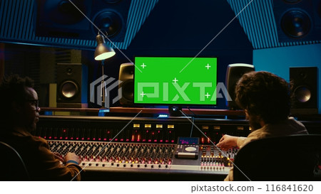 Team of music engineer and artist recording tracks on greenscreen, processing sounds to create a new song. Musician working closely with producer to make high quality tunes. Camera A. 116841620