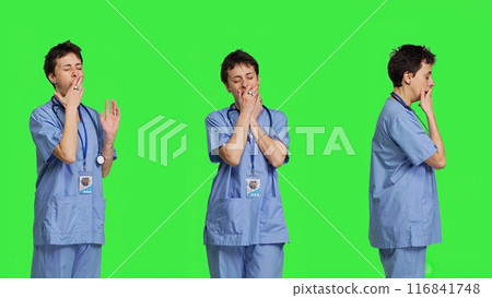 Medical assistant feeling extremely sleepy against greenscreen backdrop, being overworked after the night shift. Woman nurse yawns and feels exhausted in studio, burnout and anxiety. Camera B. 116841748
