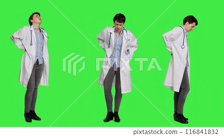 Woman physician experiencing lower back acute pain in studio, suffering from scoliosis and having muscles discomfort. Medic dealing with backache from burnout, greenscreen backdrop. Camera A. Woman physician experiencing lower back acute pain in studio, suffering from scoliosis and having muscles discomfort. Medic dealing with backache from burnout, greenscreen backdrop. Camera A. 116841832