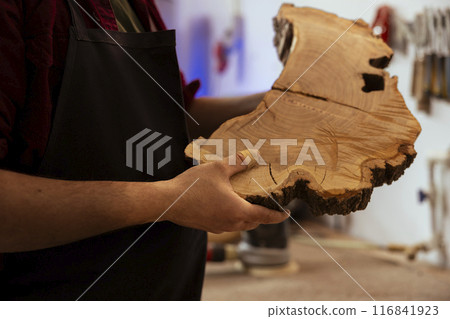 Man in woodworking shop inspecting lumber piece before assembling furniture, checking for scratches. Cabinetmaker evaluating timber block, ensuring it meets quality standards, close up shot Man in woodworking shop inspecting lumber piece before assembling furniture, checking for scratches. Cabinetmaker evaluating timber block, ensuring it meets quality standards, close up shot 116841923