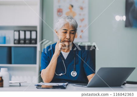 Thoughtful Hispanic female doctor sitting at her desk in a bright medical office, looking at a laptop screen. Thoughtful Hispanic female doctor sitting at her desk in a bright medical office, looking at a laptop screen. 116842363