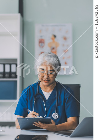 Thoughtful Hispanic female doctor sitting at her desk in a bright medical office, looking at a laptop screen. 116842365
