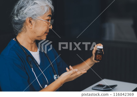 A woman doctor is writing on a clipboard and holding a bottle of pills. She is smiling and seems to be in a good mood A woman doctor is writing on a clipboard and holding a bottle of pills. She is smiling and seems to be in a good mood 116842369