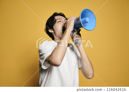 A man shouting into a megaphone against a colored background 116842616
