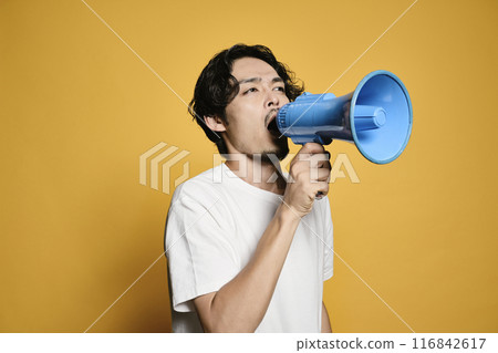 A man shouting into a megaphone against a colored background 116842617