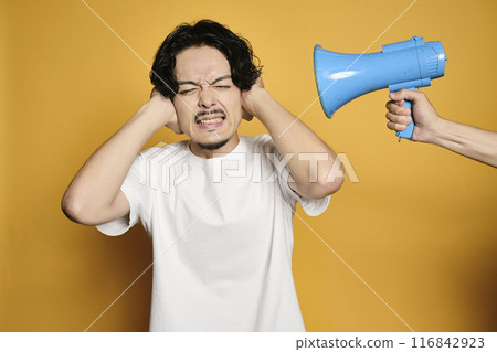 A man covering his ears from the sound of a loudspeaker in front of a colored background 116842923