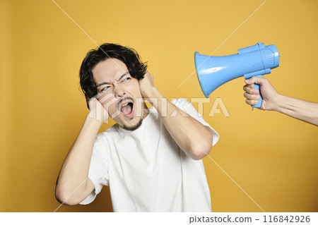 A man covering his ears from the sound of a loudspeaker in front of a colored background 116842926