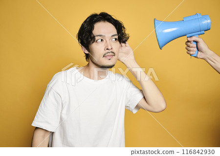 A man covering his ears from the sound of a loudspeaker in front of a colored background 116842930