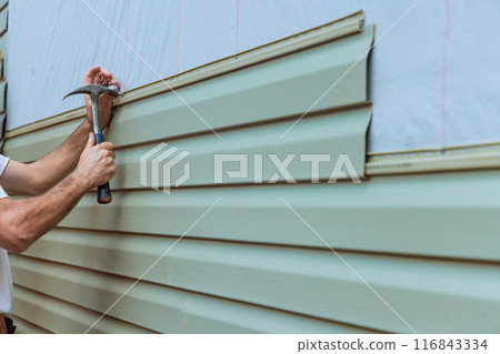 Contractor installing vinyl siding plastic panels on facade wall of new home 116843334