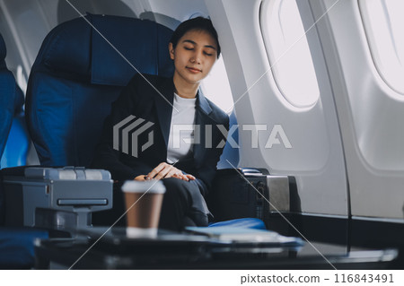 Tired young asian businesswoman eyes closed taking a nap at her seat during a flight on airplane. Transportation and business people concept. Tired young asian businesswoman eyes closed taking a nap at her seat during a flight on airplane. Transportation and business people concept. 116843491