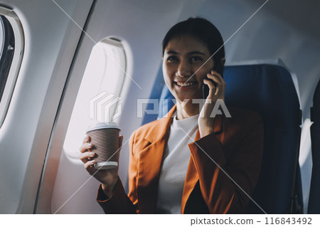 Traveling and technology. Flying at first class. Pretty young businees woman using smartphone while sitting in airplane. Traveling and technology. Flying at first class. Pretty young businees woman using smartphone while sitting in airplane. 116843492